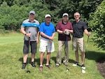 Four men in stand together holding golf clubs.