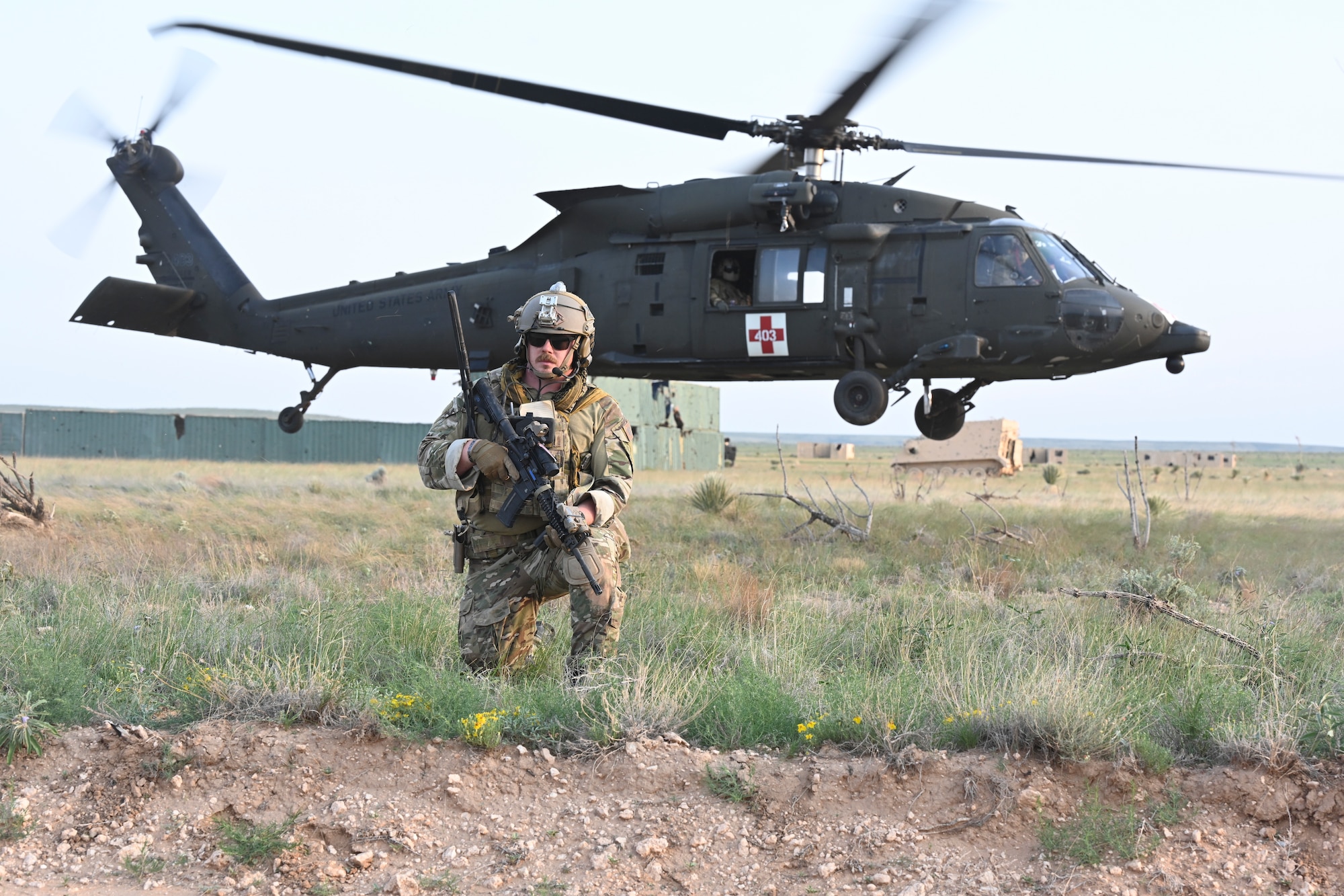An Exercise Zia Sun participant kneels as an UH-60 Blackhawk takes off on July 20, 2021, at White Sands Missile Range, New Mexico. The exercise included participants from the Air Force, U.S. Army and Canada to provide joint training on realistic combat scenarios. (U.S. Air Force photo by Airman 1st Class Adrian Salazar)