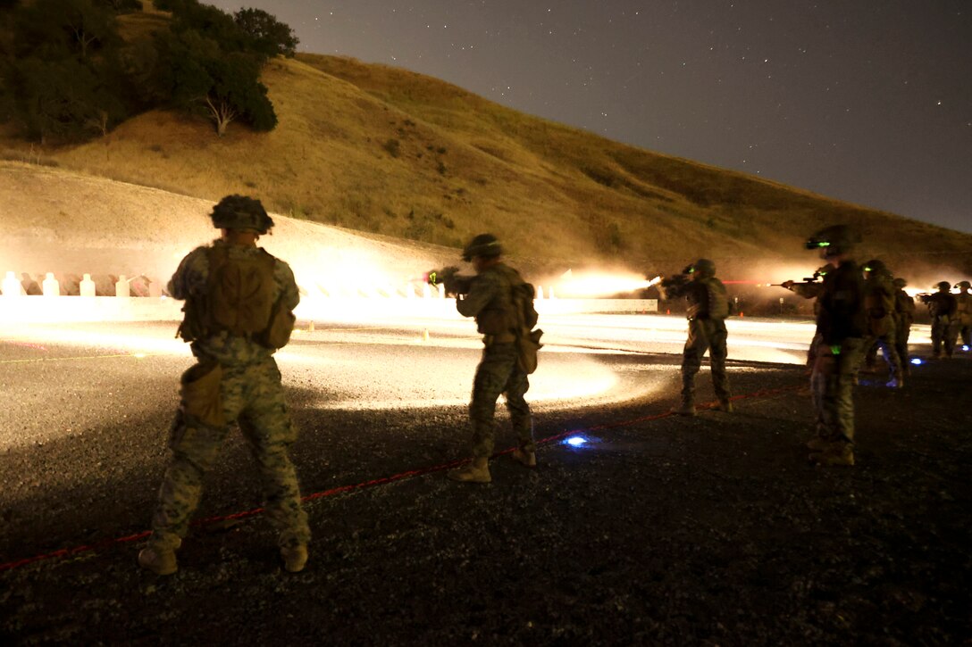 Marines fire weapons at an outdoor range, illuminating a dark sky.