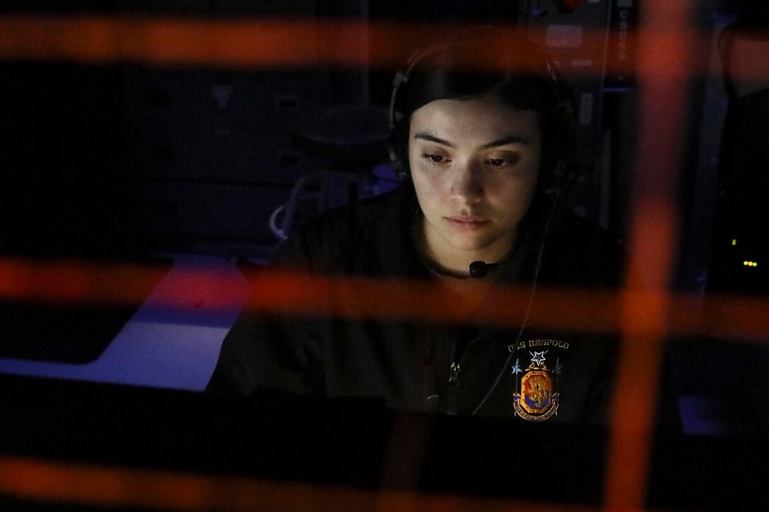 A sailor sits and looks at a screen or control panel.