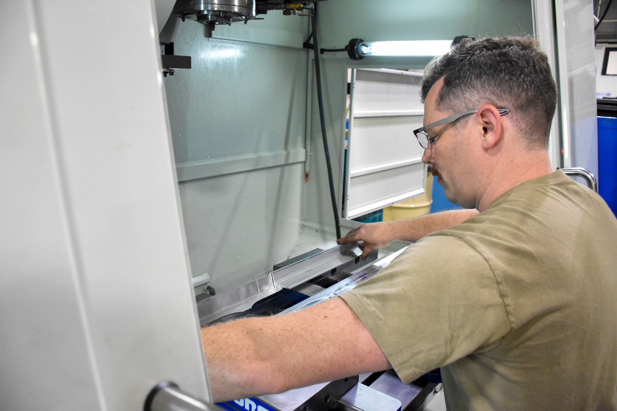 U.S. Air Force Staff Sgt. Johnathan Shellhart, a machinist with the 442d Maintenance Squadron, places a piece of stock into a CNC mill