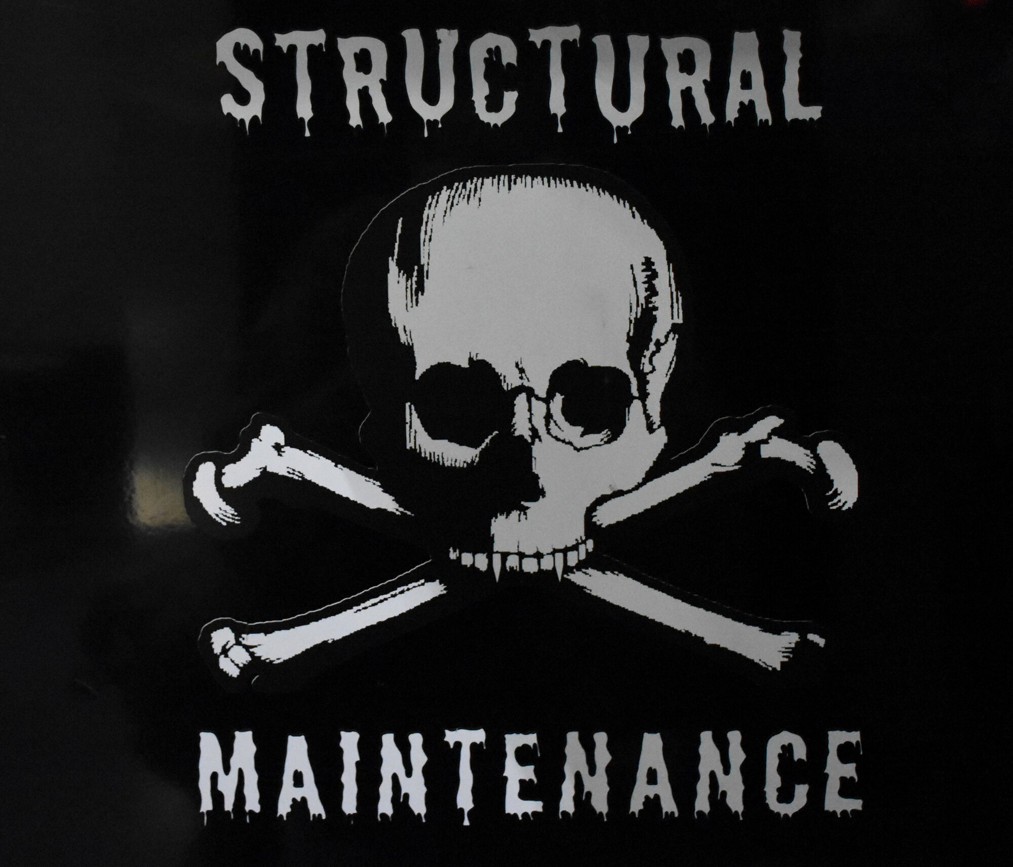 A structural maintenance sticker with a skull and crossbones on the side of a black rolling toolbox.