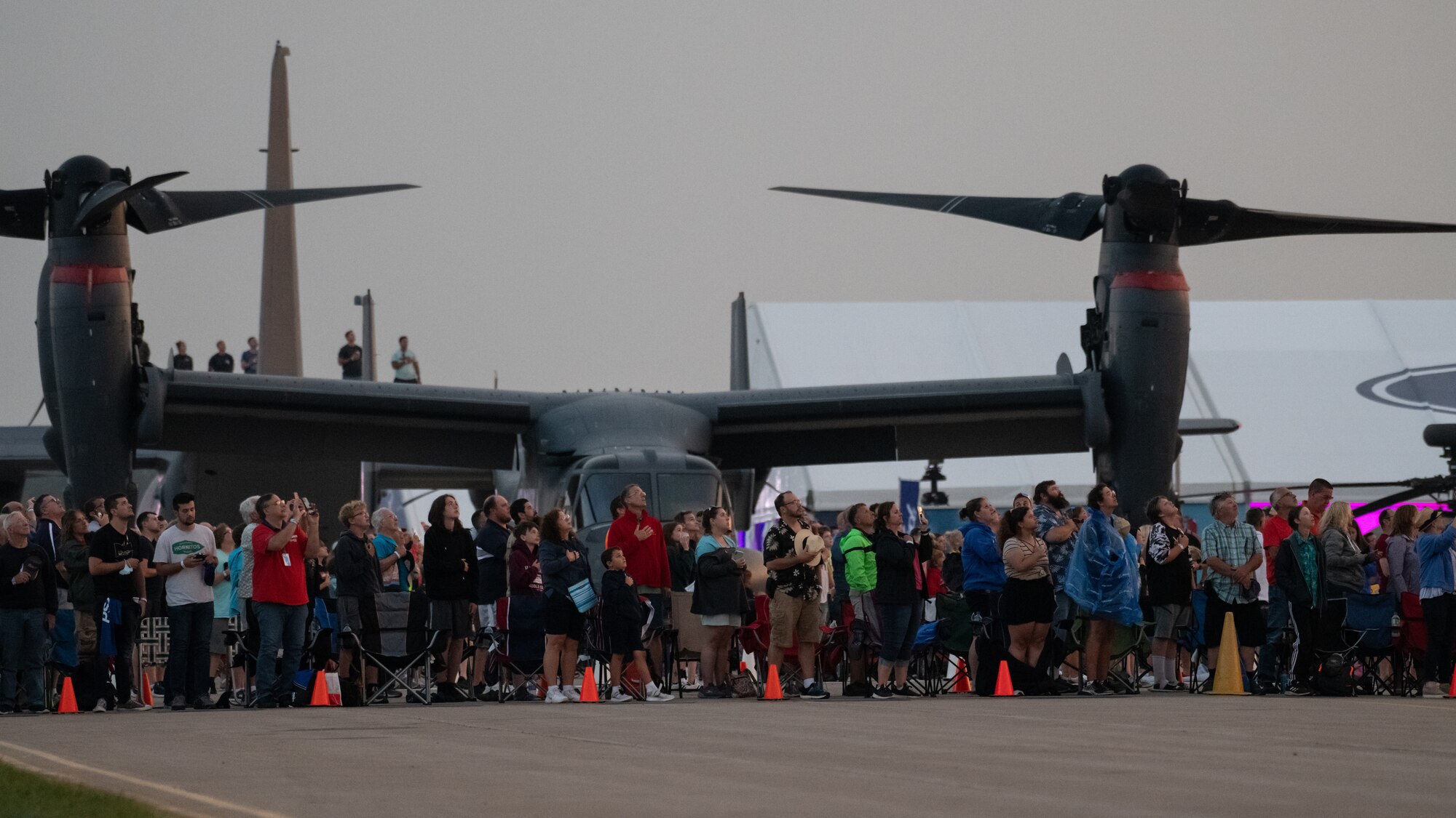 Airshow attendees stand for the national anthem during an airpower demonstration as part of EAA AirVenture Oshkosh 2021, at Wittman Regional Airport, Wis., July 31, 2021.