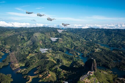 Jets fly in a V formation over mountainous terrain.