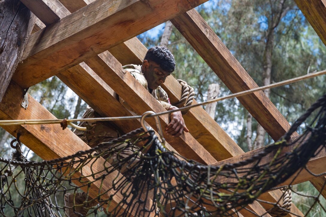 A soldier climbs through an obstacle of wooden boards.