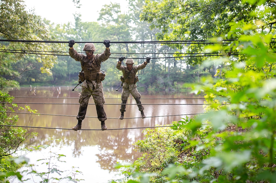 Two Marines use ropes to cross a muddy river.