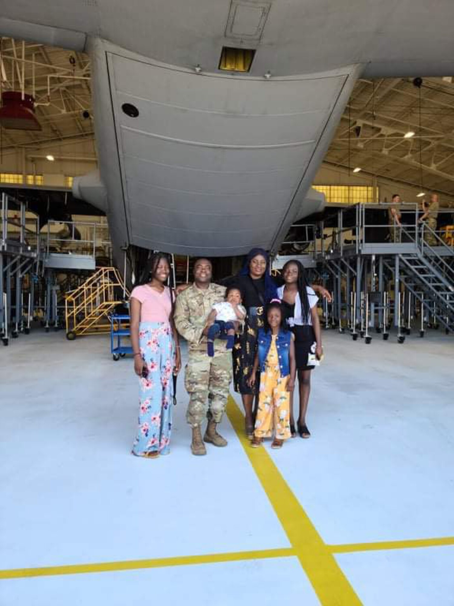 Senior Airman Ajay Vogar, 379th Expeditionary Maintenance Squadron commander support staff security manager, now deployed member at Al Udeid Air Base, Qatar, poses for a photo with his family inside of an aircraft maintenance hangar.