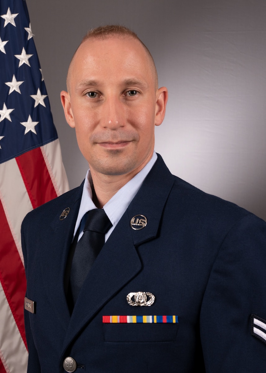 Official Photo of A1C Anthony O'Connor, audio engineer with Rhythm in Blue and the Concert Band, two of six ensembles in the Heritage of America Band, Langley AFB, VA.  A1C O'Connor in wearing blue service dress in front of an American Flag background.