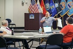 Man with microphone talking to man and woman in a conference room.