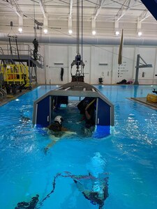 Petty Officer First Class Cody Dodd and several other Sailors are lowered underwater in a simulated airframe crew compartment before attempting to safely egress during the “Helo Dunker” course. The METS Trainer (also known as the Helo Dunker) is designed to provide a realistic environment in which trainees can practice procedures for evacuation from ditched aircraft. The METS training system is designed to provide hands-on training in underwater egress from multi-place aircraft. The training is general in nature, but the METS can be configured specific to aircraft type. The METS incorporates the use of exterior cutout exit panels as well as escape exit panels that replicate actual helicopter escape exits.