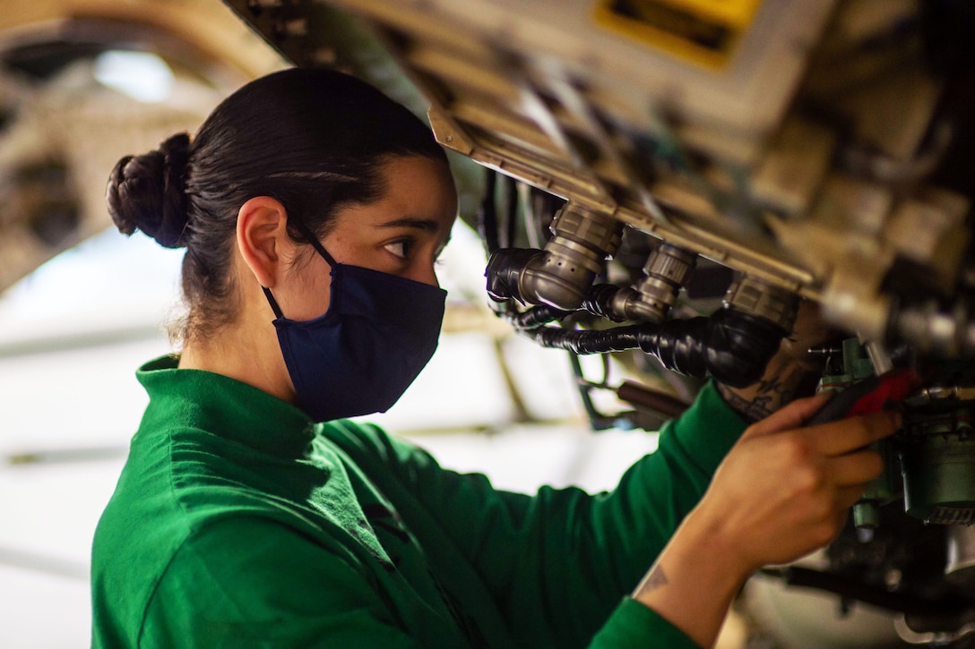 A sailor wearing a face mask conducts maintenance on an aircraft.