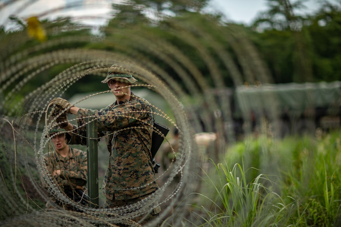 A Marine handles barbed wire forming a barricade outdoors.