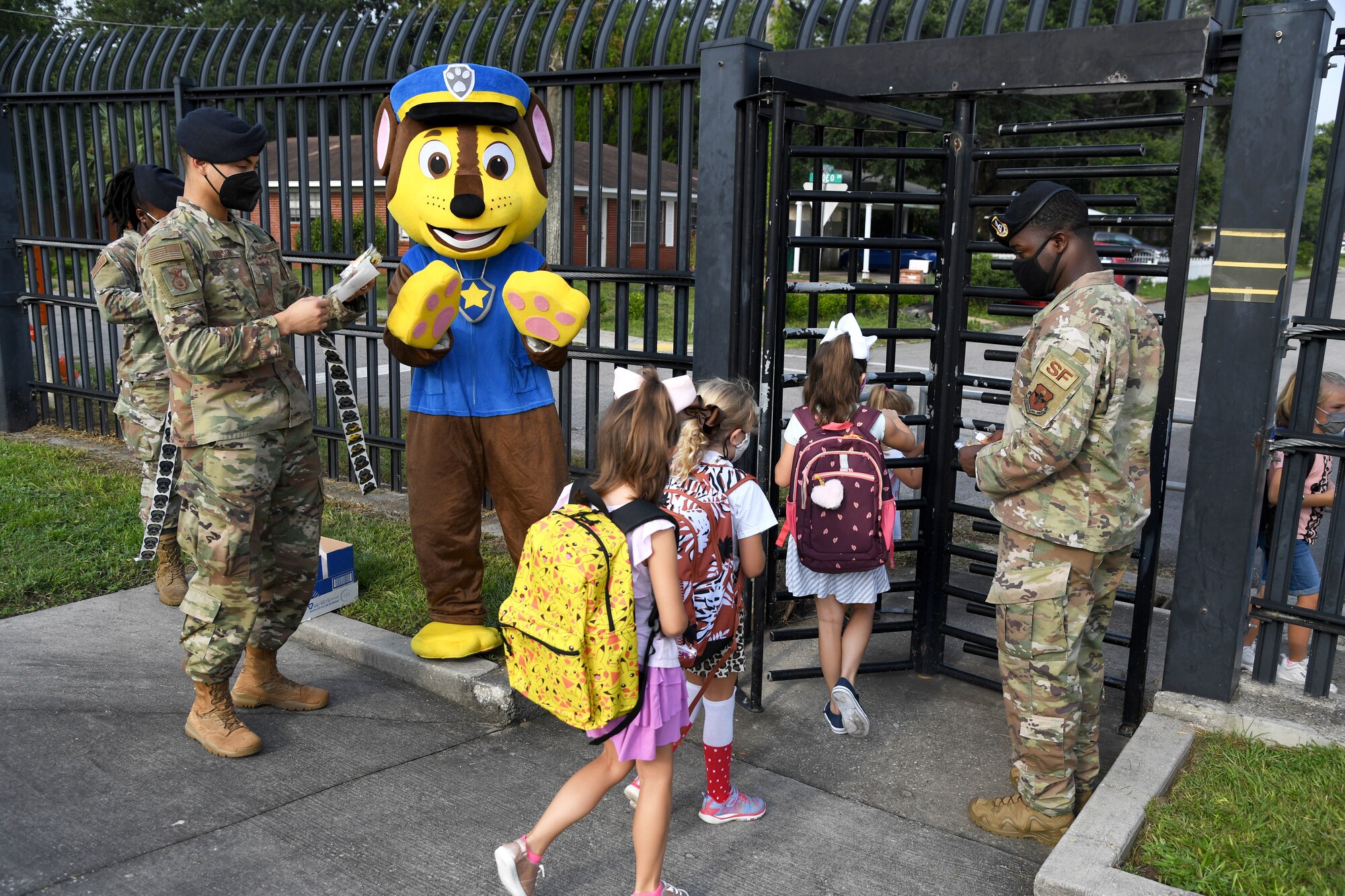 Members of the 81st Security Forces Squadron and Chase the Paw Patrol dog greet military children for the first day of school near the pedestrian gate at Keesler Air Force Base, Mississippi, Aug. 4, 2021. Defenders welcomed the children with stickers as they went to Jeff Davis Elementary School. (U.S. Air Force photo by Kemberly Groue)