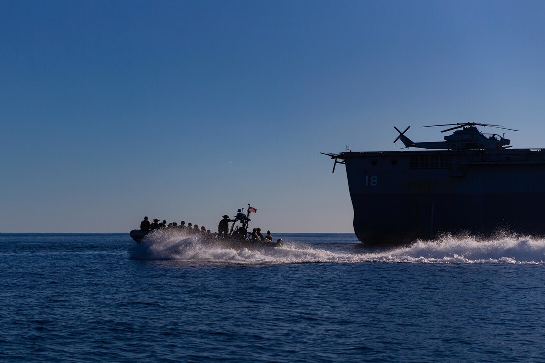 Marines travel in a raft next to a ship in blue waters.