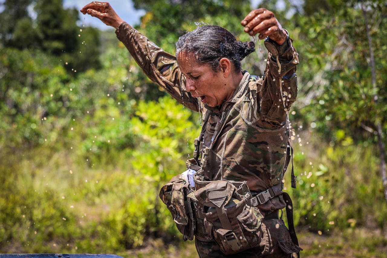 A soldier holds arms up as water drips from her saturated uniform.