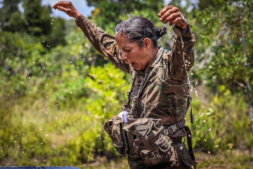 A soldier holds arms up as water drips from her saturated uniform.