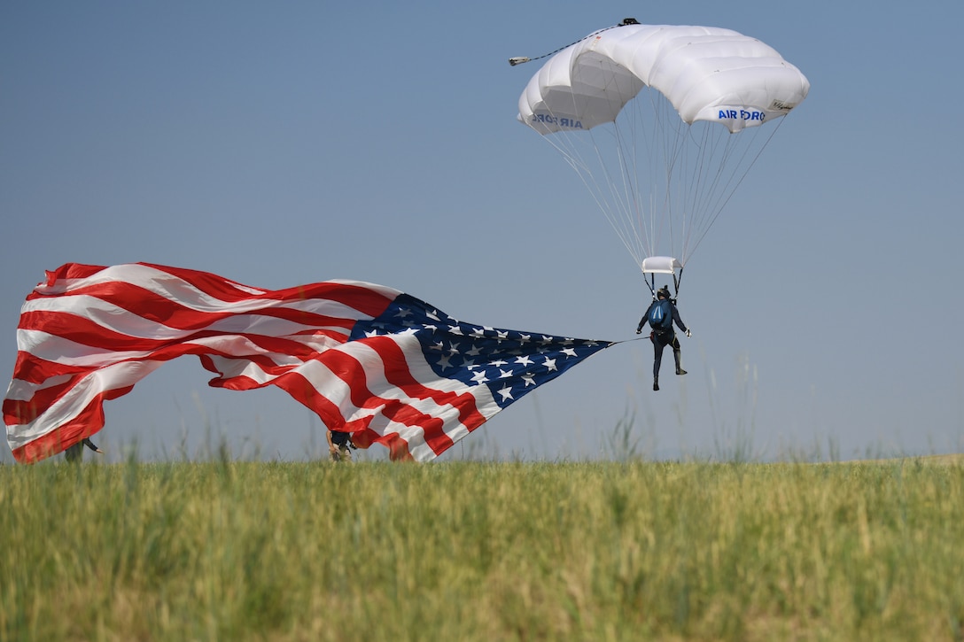 An Air Force skydiver prepares to land on flat ground alongside a billowing American flag.