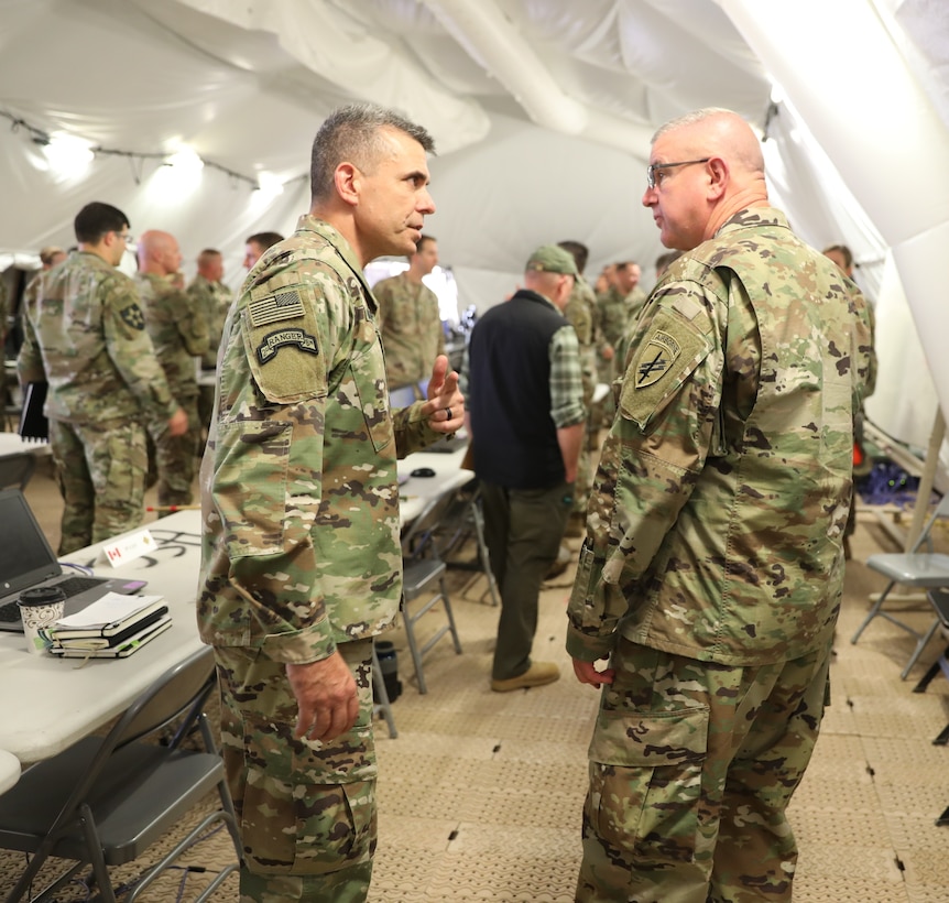 Brig. Gen. Gen. Jeffrey C. Coggin (left), commanding general of the U.S. Army Civil Affairs and Psychological Operations Command (Airborne), speaks with Maj. Gen. Matthew McFarlane, commanding general, 4th Infantry Division, as they participate in the Joint Warfighting Assessment 2021 distinguished visitor day initial briefing at Fort Carson, Colo., June 25, 2021. U.S. Army Civil Affairs and Psychological Operations Command (Airborne) Civil Affairs, Psychological Operations, and Information Operations Soldiers took part in JWA 2021 with participants from different Army units and multinational partners such as U.K., Australian and Canadian armed forces, working to improve interoperability between U.S. joint forces and our allies. JWA exercises help the Army evaluate emerging concepts, integrate new technologies, and promote interoperability between the Army, other services and, our multinational partners. Joint and multinational partners are key to the success of Multi-Domain Operations.