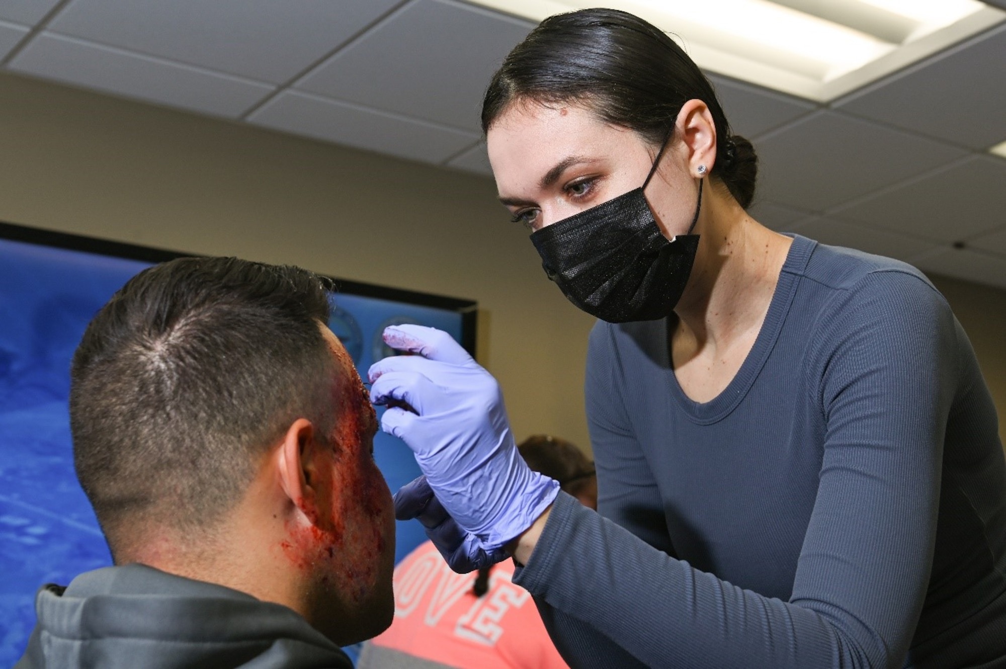 Tech. Sgt. Katsiaryna Durant, 6th Refueling Wing dental hygienist, applies stage blood to Petty Officer 2nd Class Jason Santa Maria, USS Constitution Boatswain mate,  to create a severe trauma simulation prior to a Ready Eagle exercise at Hanscom Air Force Base, Mass., July 30. Fifty volunteers donned moulage to authenticate the 66th Medical Squadron training event. (U.S. Air Force photo by Todd Maki)