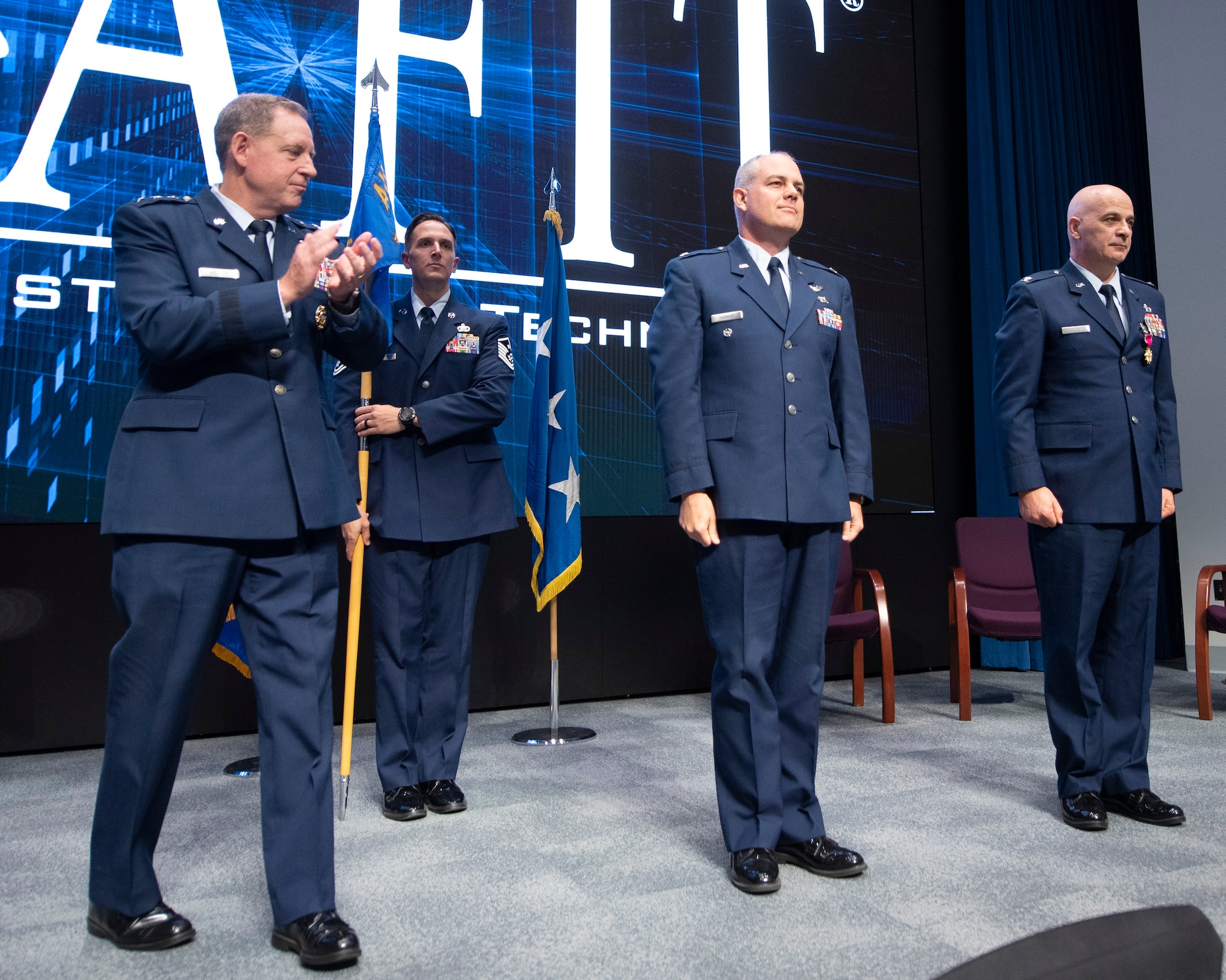 Col. Paul Harmer (center), Air University Detachment 1 commander at the Air Force Institute of Technology, receives applause from Lt. Gen. James Hecker, Air University commander and president, and the audience during a change-of-command ceremony July28 at the Wright-Patterson Air Force Base campus. Harmer assumes AFIT command from Col. Paul Cotellesso (right), who retired following 30 years of Air Force service. (U.S. Air Force photo by R.J. Oriez)