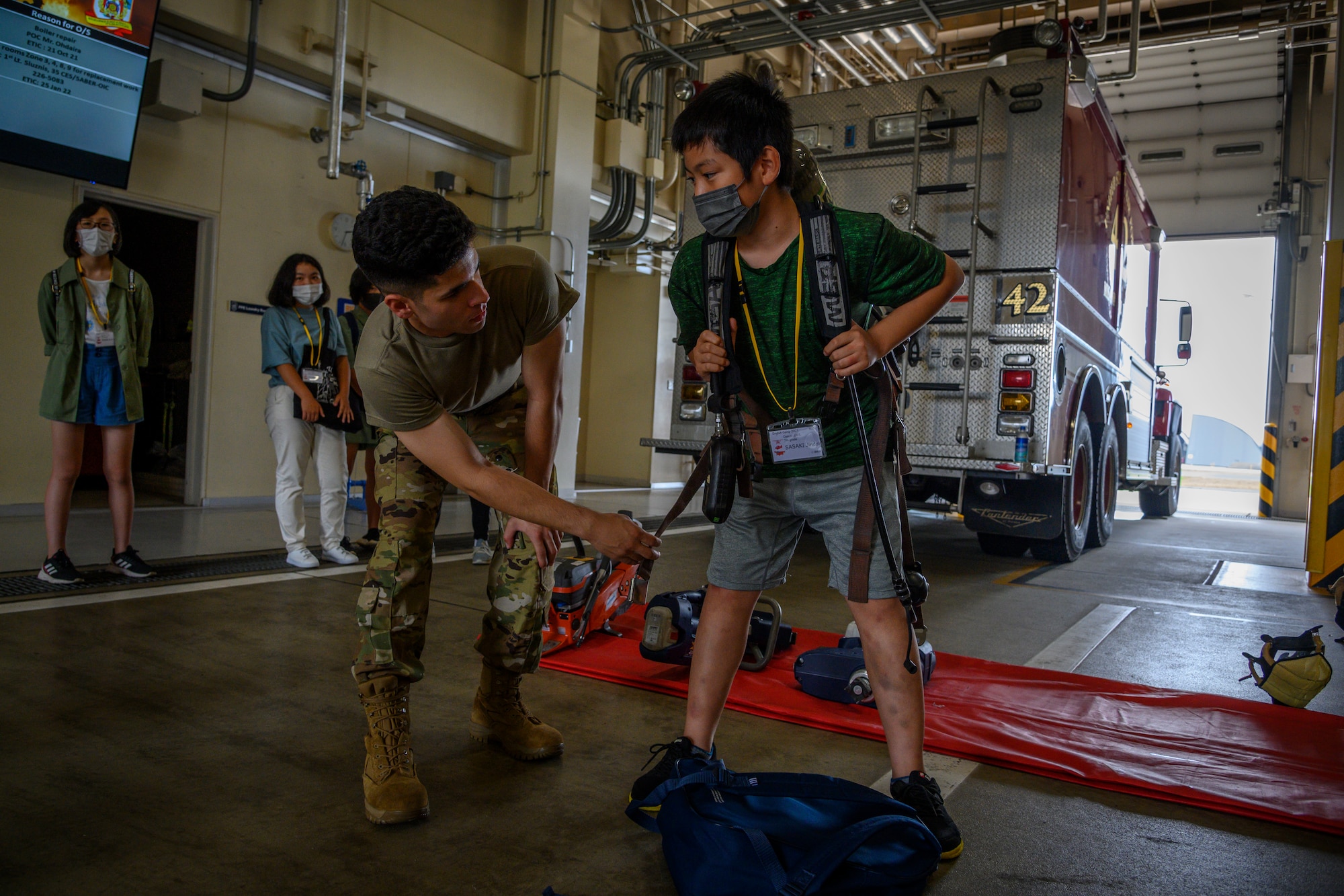 A Misawa City English Camp student dons gear during a base tour at Misawa Air Base, Japan, Aug. 3, 2021. While on the tour, students watched a 35th Civil Engineer Squadron firefighter don fire equipment for the first time and were able to don equipment themselves. (U.S. Air Force photo by Senior Airman China M. Shock)