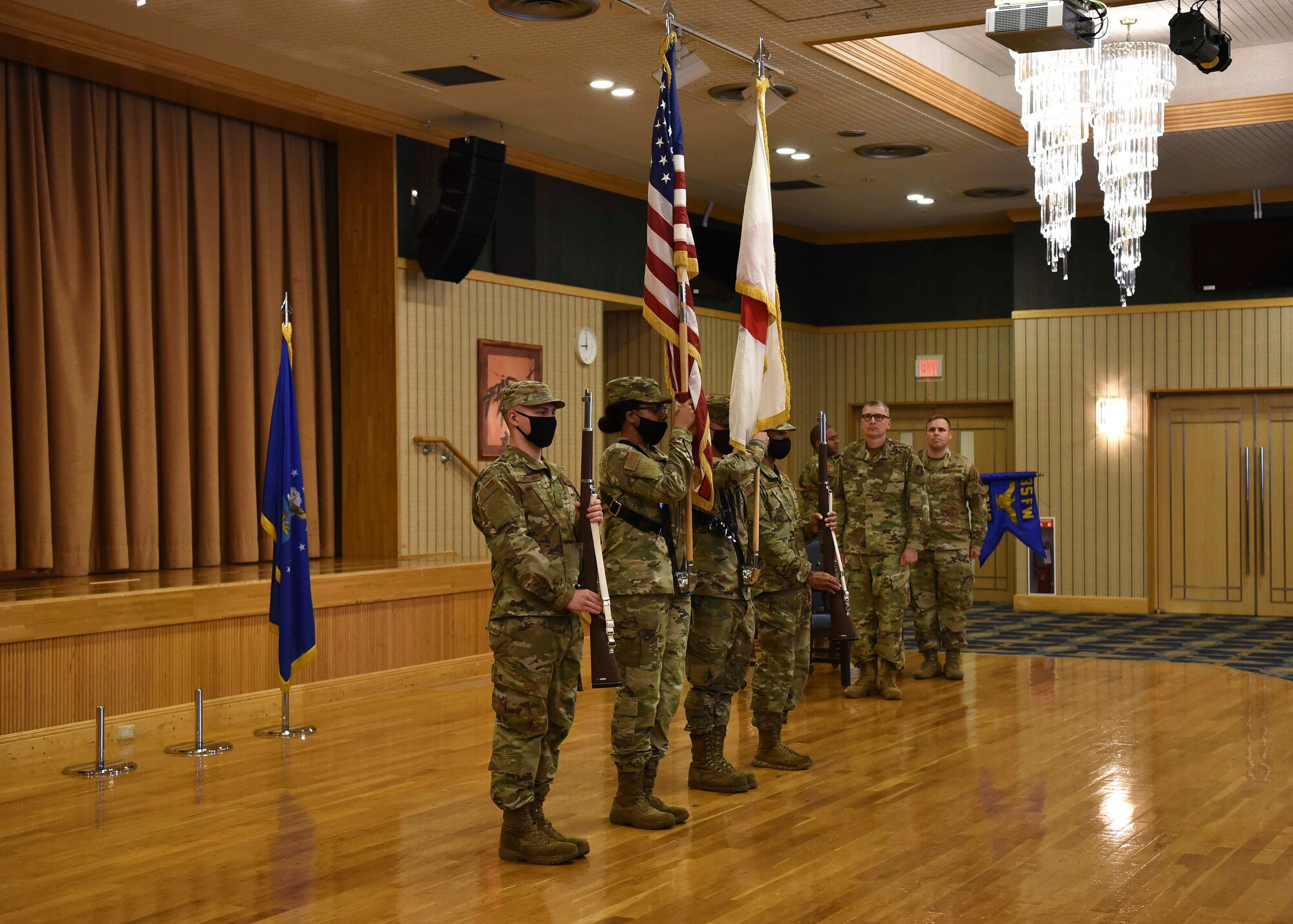 Military members hold flags and rifles as others salute.