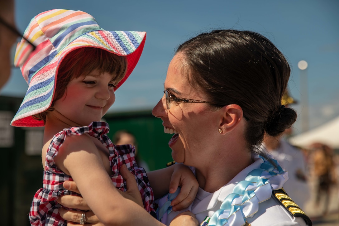 A Navy officer smiles as she holds her daughter in her arms.