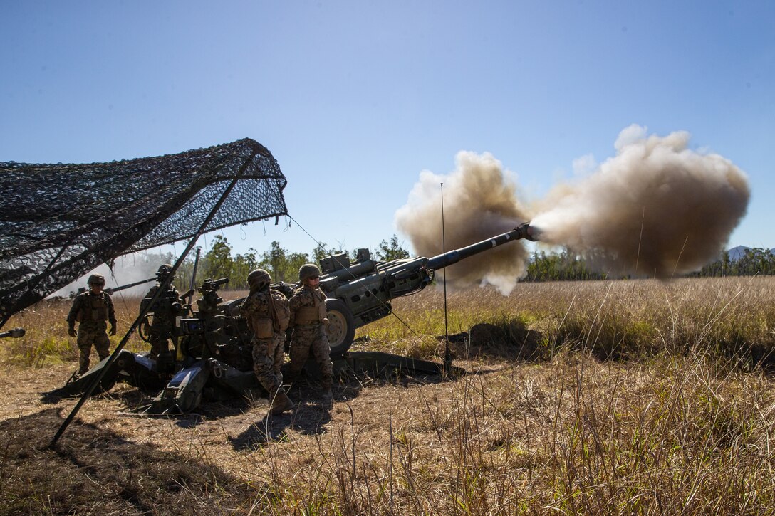 A group of Marines fire a howitzer in a large field.
