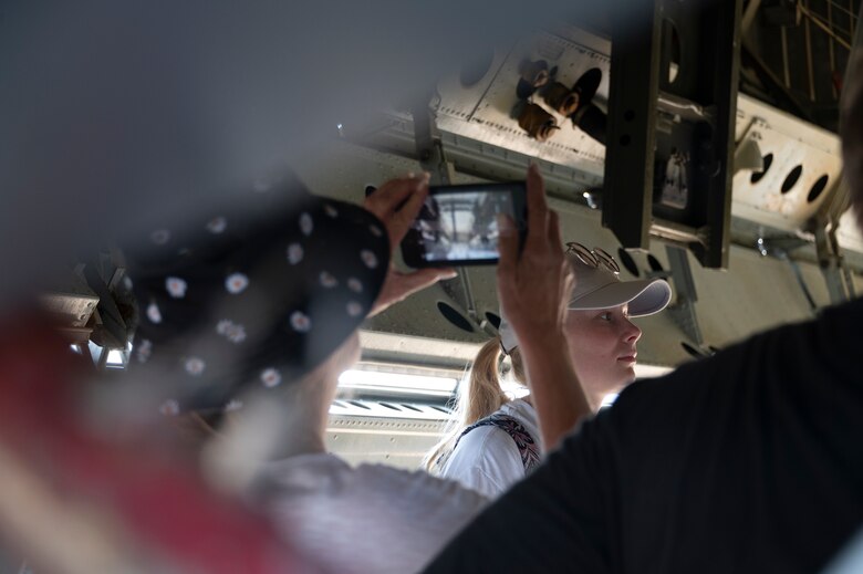 A woman photographs another woman inside the bomb bay of a bomber aircraft.
