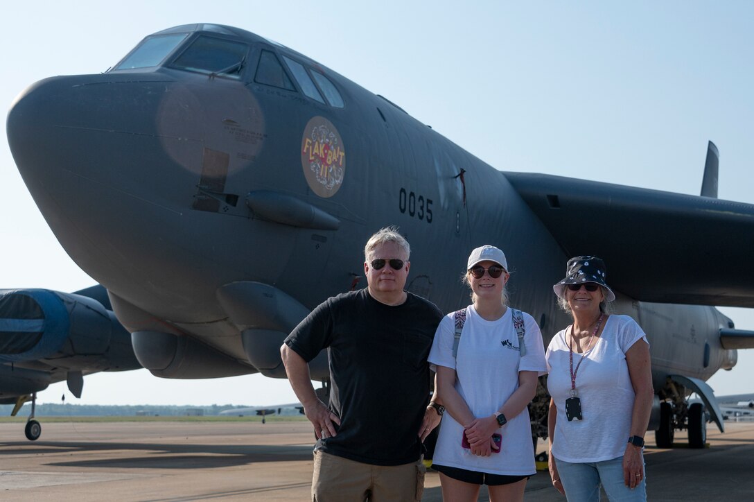 Three people stand smiling in front of an aircraft.