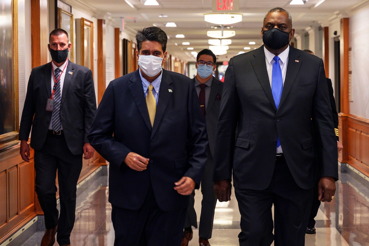 Four men walk down a hallway.