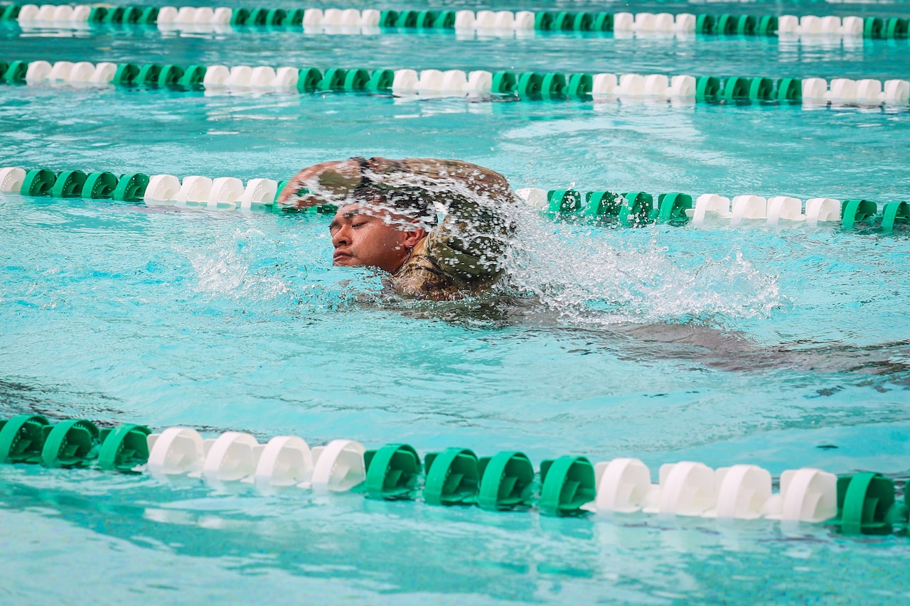 A soldier swims freestyle in a pool.