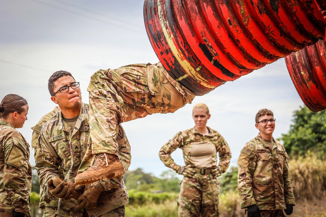 A soldier emerges feet first from a raised tube as a fellow soldier helps the first one out.