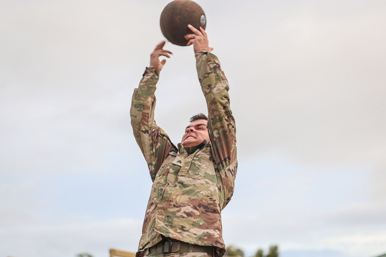 A soldier reaches both arms up toward a rubber ball.