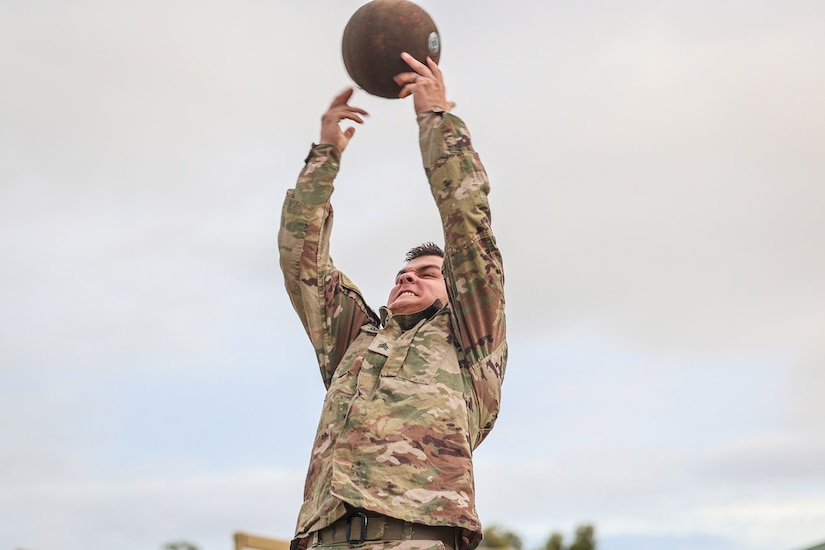 A soldier reaches both arms up toward a rubber ball.