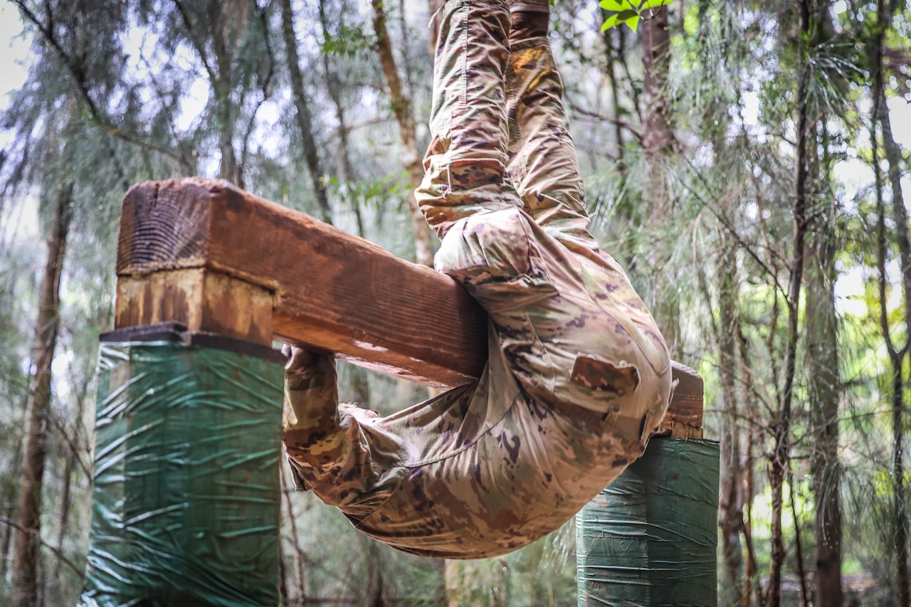 A soldier flips over a raised wooden plank in a wooded area.