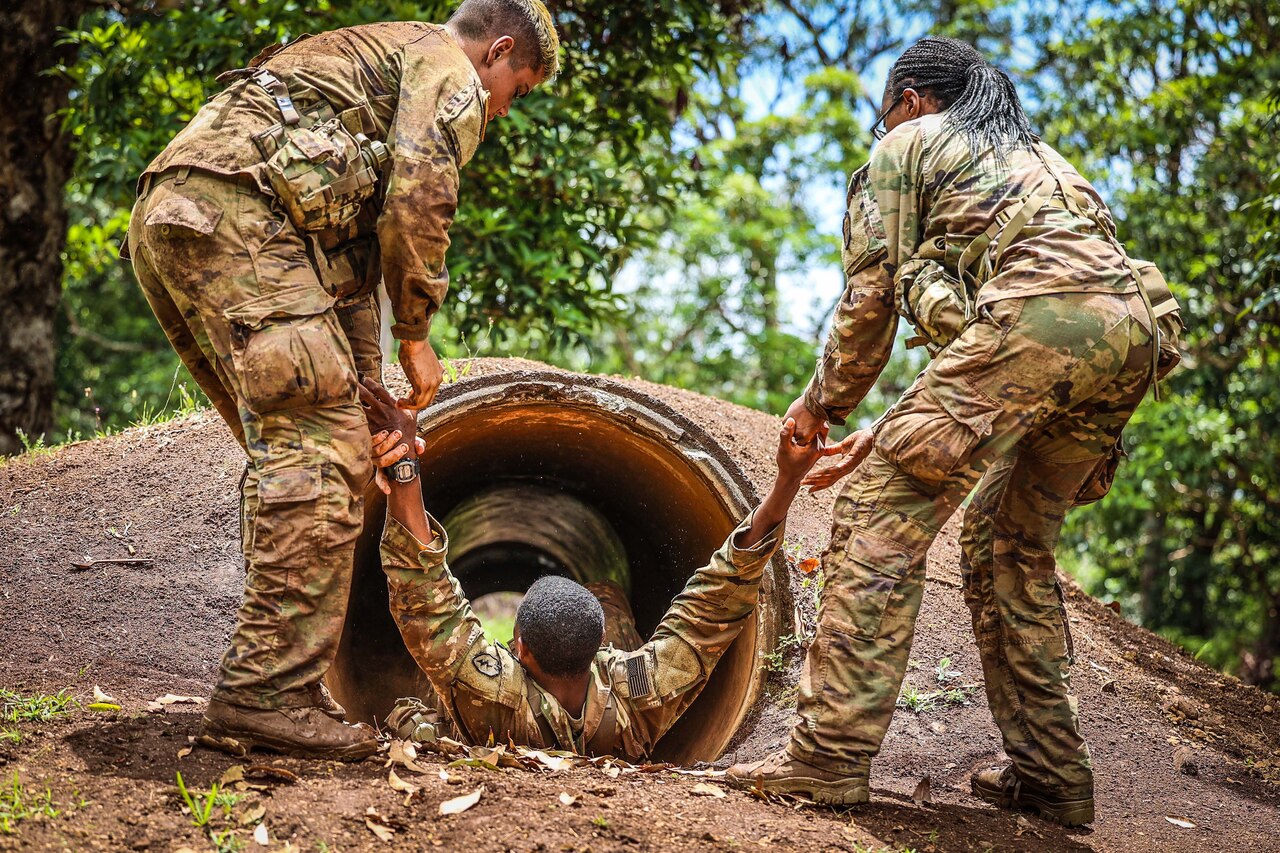 Two soldiers pull a third one through a tunnel on the the ground.