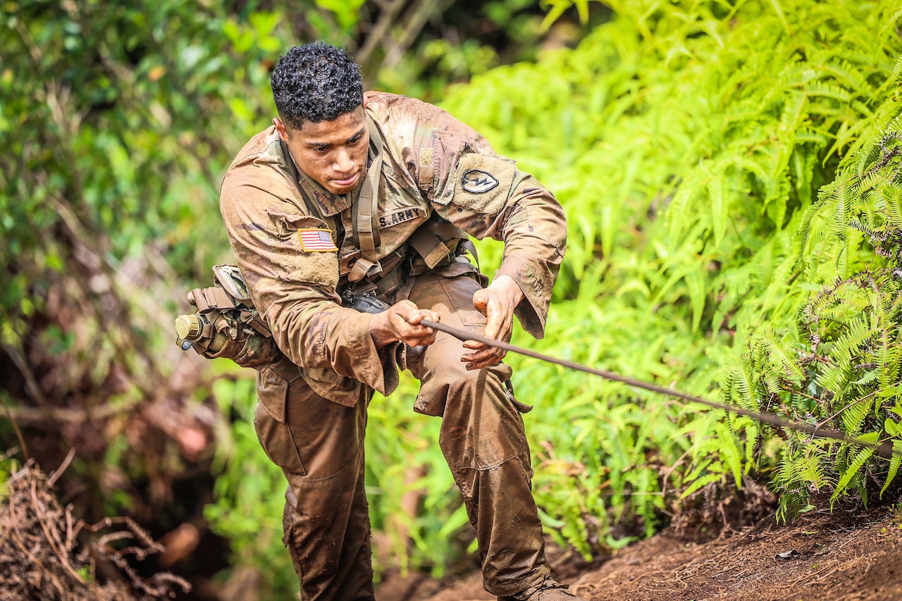 A soldier climbs a hill using a rope.