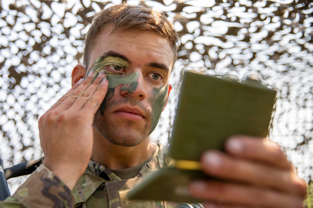 A soldier holds up a small mirror while appling camo face paint .