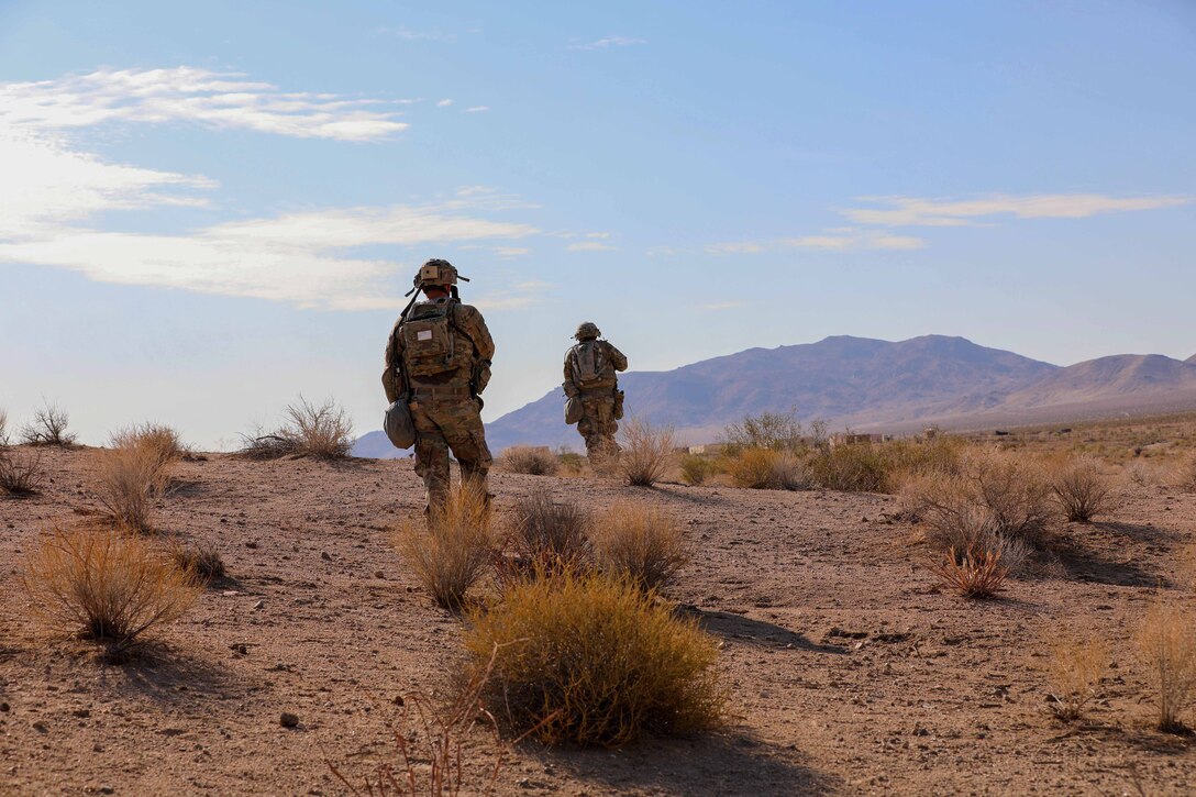 Two soldiers walk over desert terrain.