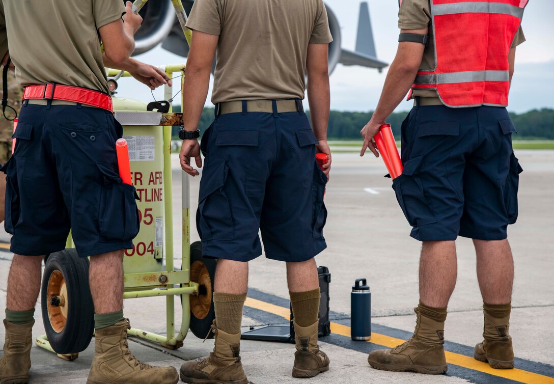 Airmen from the 736th Aircraft Maintenance Squadron prepare to marshal a C-17 Globemaster III for take off at Dover Air Force Base, Delaware, Aug. 4, 2021. According to the modifications of Air Force Instruction 36-2903, maintenance commanders can now authorize Airmen to wear dark blue shorts in place of the Operational Camouflage Pattern trousers when temperatures are expected to meet or exceed 80 degrees Fahrenheit. (U.S. Air Force photo by Senior Airman Stephani Barge)