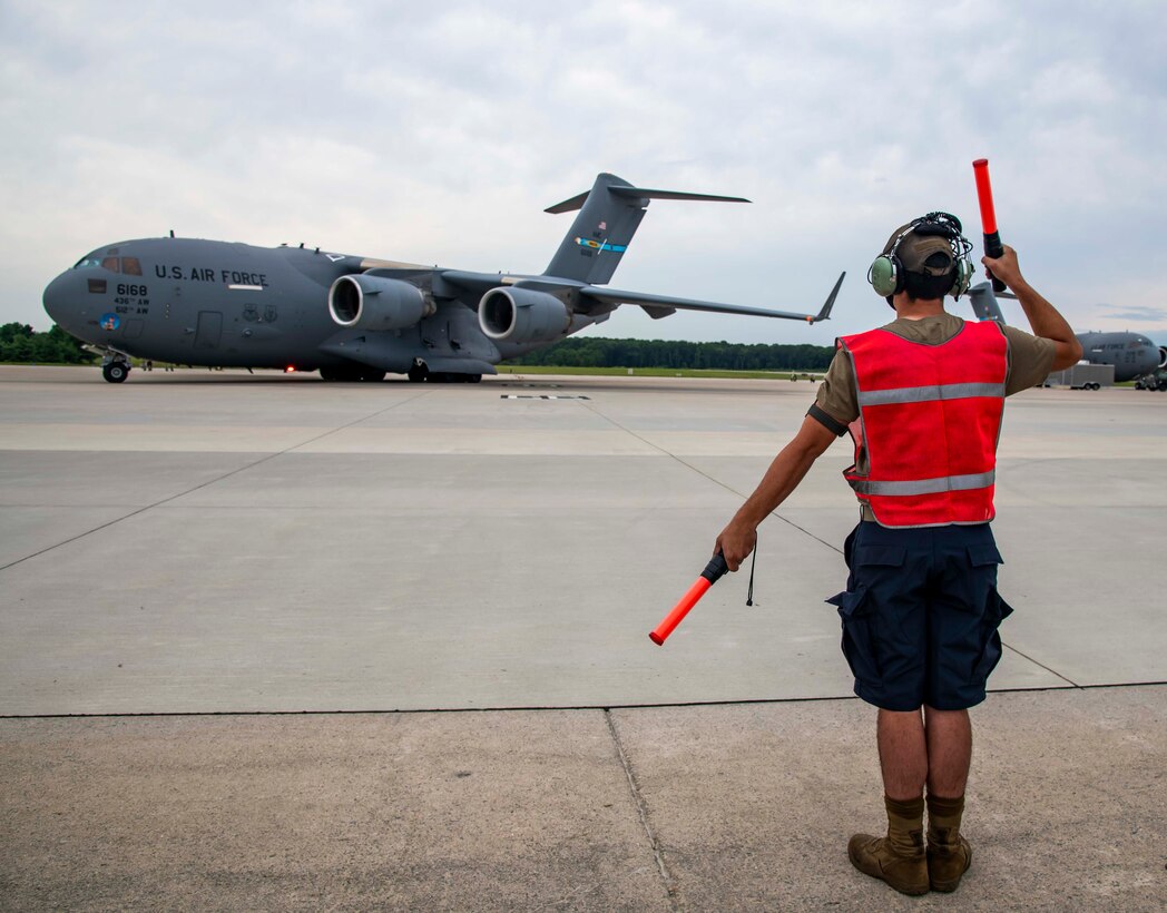 Airman Noah Mills, 736th Aircraft Maintenance Squadron assistant dedicated crew chief, marshals a C-17 Globemaster III for take off at Dover Air Force Base, Delaware, Aug. 4, 2021. According to the modifications of Air Force Instruction 36-2903, maintenance commanders can now authorize Airmen to wear dark blue shorts in place of the Operational Camouflage Pattern trousers when temperatures are expected to meet or exceed 80 degrees Fahrenheit. (U.S. Air Force photo by Senior Airman Stephani Barge)