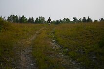 A Special Tactics operator from the 24th Special Operations Wing walks up a hill in order to receive radio signal while surveying and preparing a closed section of U.S. Highway 32 to land and receive aircraft during exercise Northern Strike 21 Aug. 5, 2021, at Alpena, Mich. Special Tactics Airmen are the Air Force’s special operations ground force, experienced in conducting global access missions such as establishing austere landing zones around the world.   (U.S. Air Force photo by Staff. Sgt Ridge Shan)
