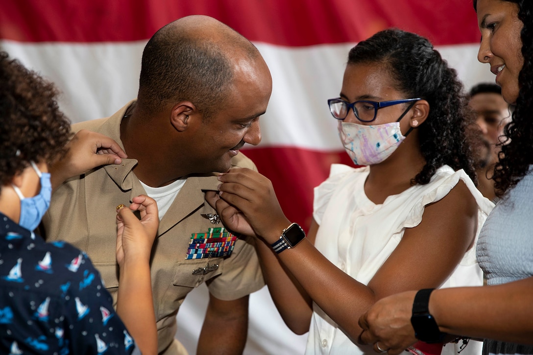 A group of people, some wearing masks, put pins on the lapel of a sailor.