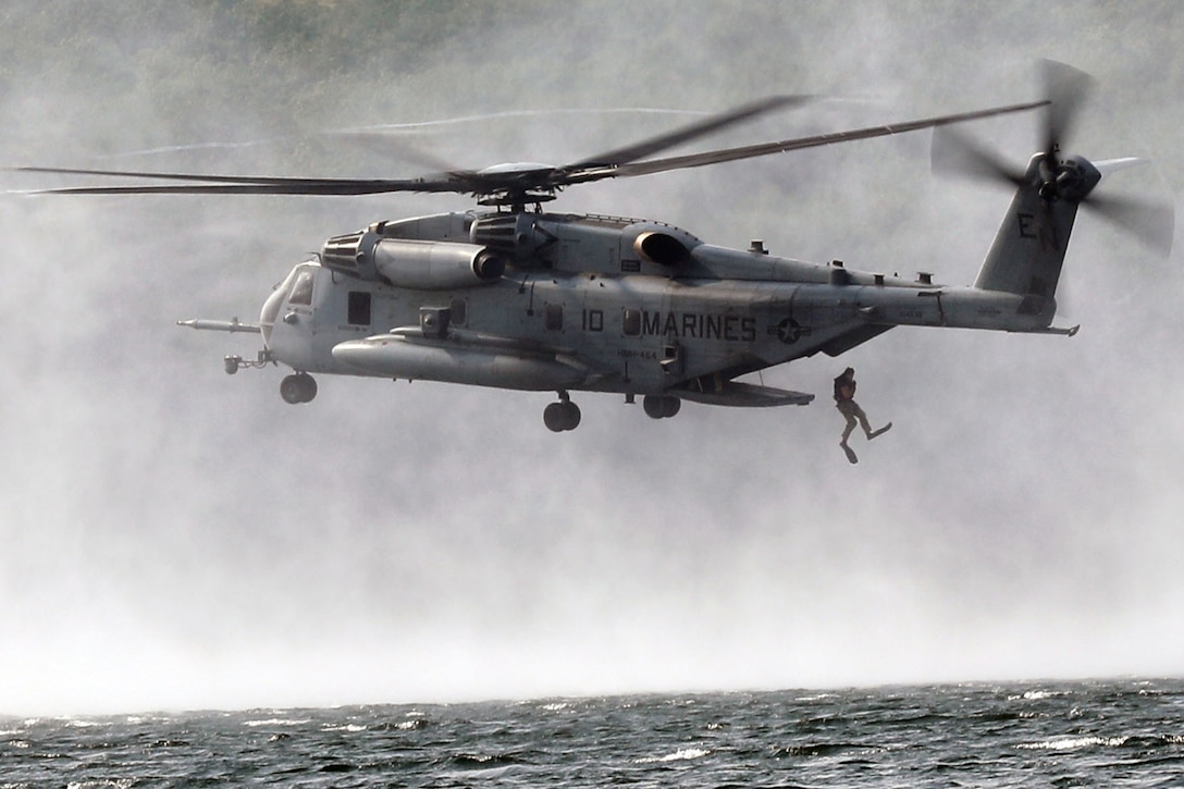 A person jumps out of the back of a low-flying helicopter into the water.