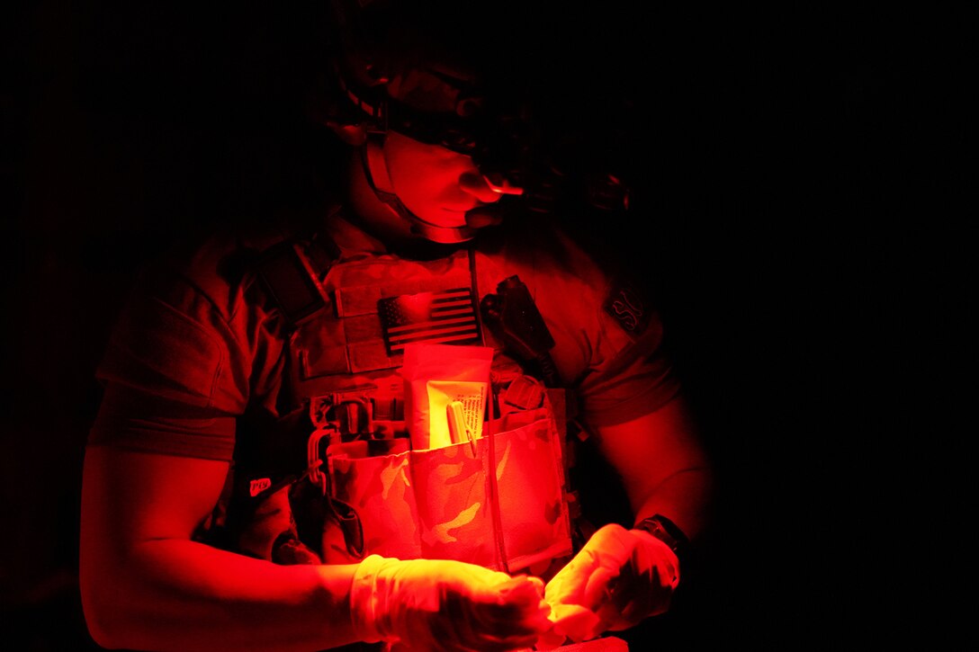 A man wearing plastic gloves prepares medical equipment under a red light.