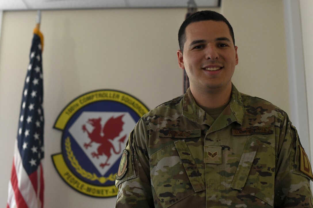 U.S. Senior Airman Jake Pineiros, 100th Comptroller Squadron finance technician poses in front of the squadron emblem Aug. 3, 2021 at Royal Air Force Mildenhall, England. (U.S. Air Force Photo by Senior Airman Antonia Herrera)
