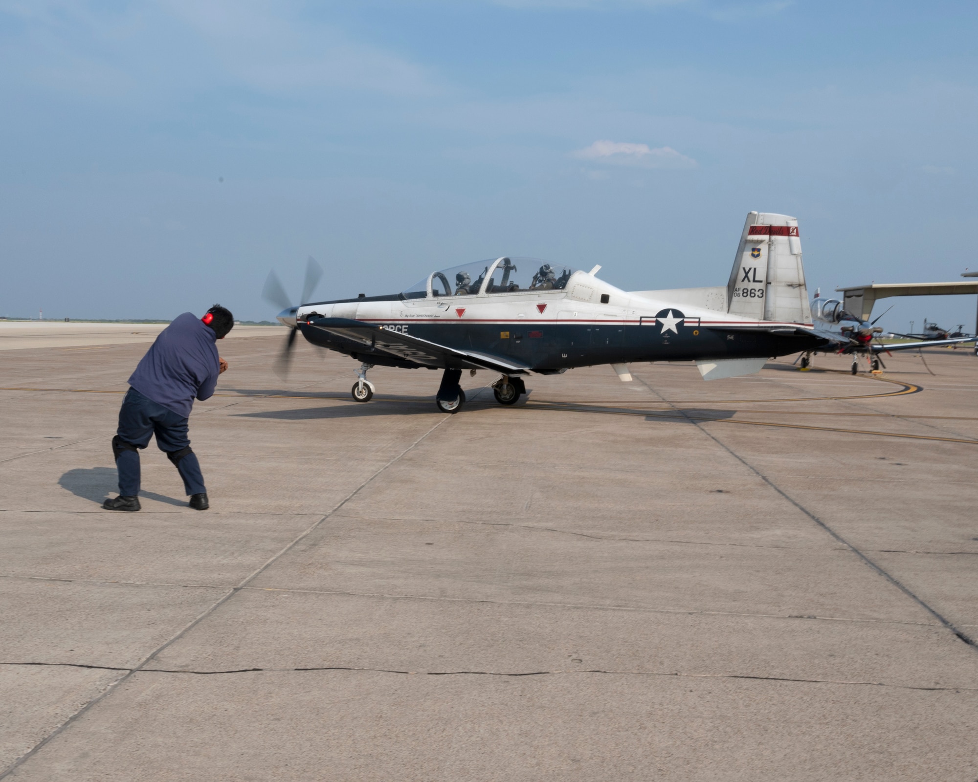 A Ground Crew member at Laughlin Air Force Base, Texas, waves through a T-6 Texan II with U.S. Air Force 2nd Lt. Christopher Ugale, a student pilot with the 47th Student Squadron Squadron and U.S. Air Force Capt. Sarah Fotsch in the pilot and co-pilot seats for 2nd Lt. Ugale’s Dollar Ride on August 4, 2021.  The Dollar Flight is the first flight in a real aircraft for a student pilot and marks a major milestone in the career of a pilot. (U.S. Air Force Photo by Senior Airman Nicholas Larsen)
