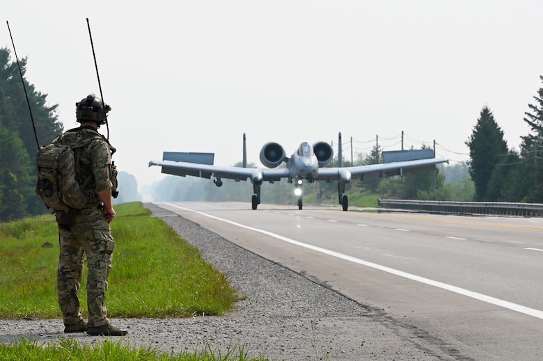 A special tactics operator from the 24th Special Operations Wing guides an A-10 Thunderbolt II from the Michigan Air National Guard's 127th Wing as it lands on a closed public highway Aug. 5, 2021 at Alpena, Mich., as part of a training exercise during Northern Strike 21. This is the first time in history that the Air Force has purposely landed modern aircraft on a civilian roadway in the U.S. The joint training event tested part of the agile employment concept, focusing on projecting combat power from austere locations. (U.S. Air Force photo by Staff Sgt. Ridge Shan)