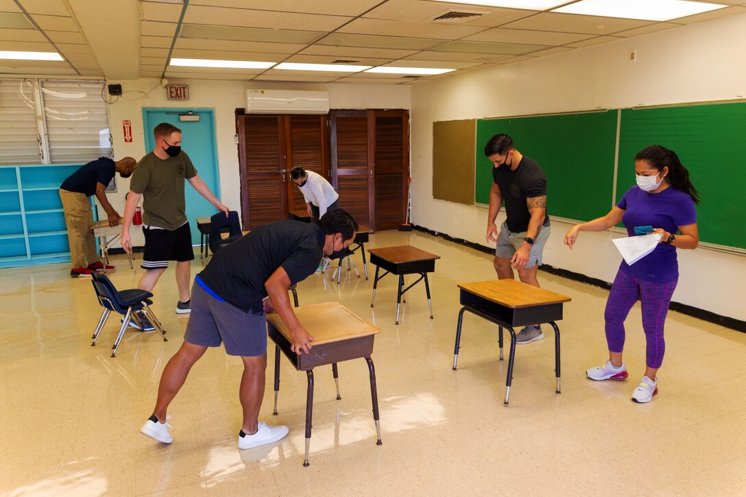 Six people wearing face masks move desks and chairs into rows inside a classroom.
